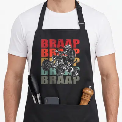 Four racing apron - White ATV rider outline over red orange yellow and green BRAAP text stack — shown on a black cotton canvas apron against a white background