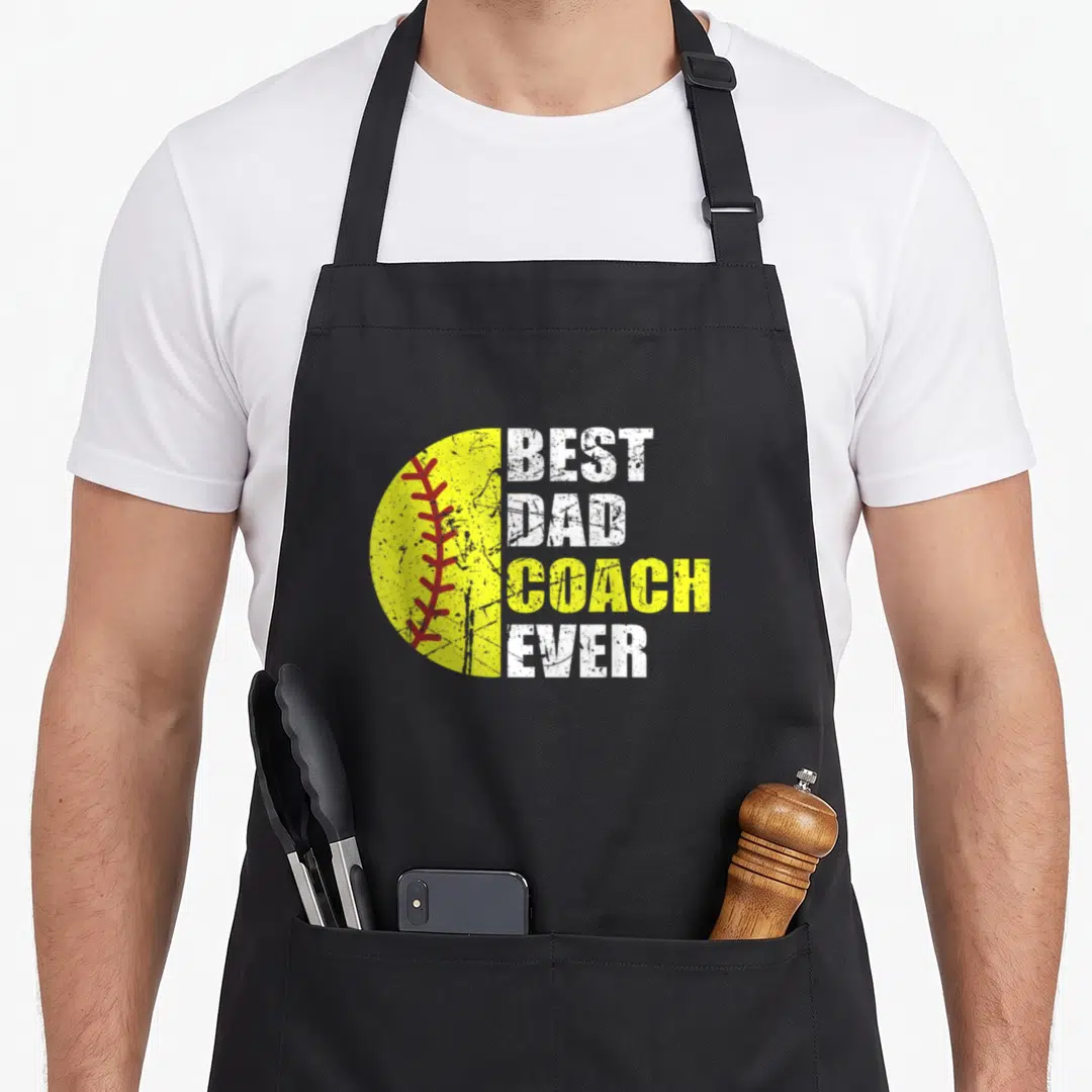 Coach softball dad apron - Yellow half softball graphic with red stitching next to stacked white and yellow text — shown on a black cotton canvas apron against a white background