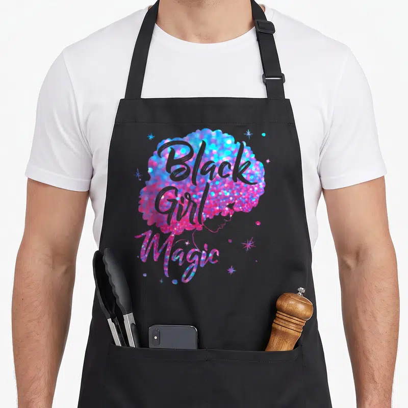 Funny magic apron - Glittery afro in blue pink magenta with Black Girl Magic text and scattered stars — shown on a black cotton canvas apron against a white background