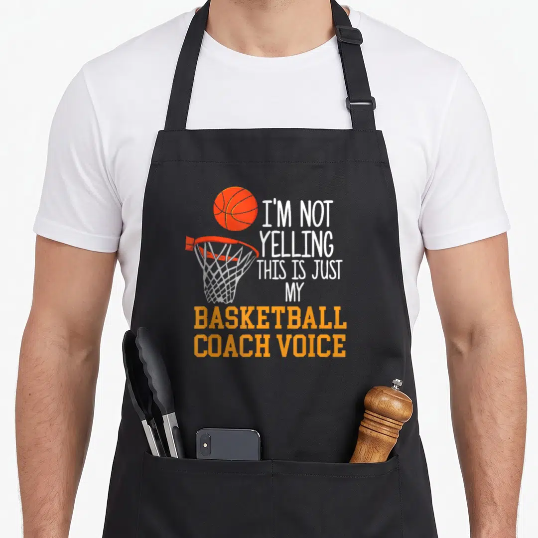 Voice coach apron - Orange basketball and hoop with white and orange text reading I'm not yelling my basketball coach — shown on a black cotton canvas apron against a white background