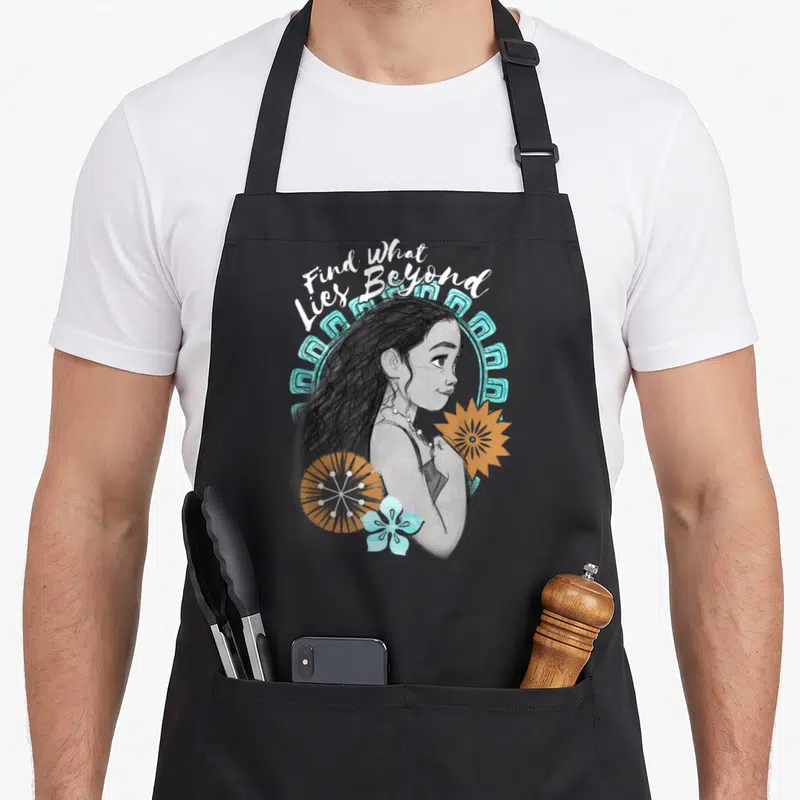 Lie beyond apron - Woman in profile with Find What Lies Beyond text and blue orange flowers — shown on a black cotton canvas apron against a white background