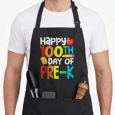 Smarter day pre k apron - Stacked text Happy 100TH DAY OF PRE-K with red apple, yellow pencil, and book in cartoon art — shown on a black cotton canvas apron against a white background