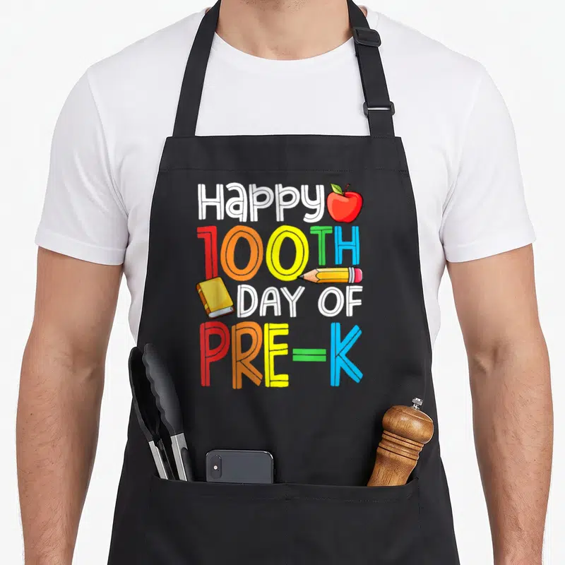 Smarter day pre k apron - Stacked text Happy 100TH DAY OF PRE-K with red apple, yellow pencil, and book in cartoon art — shown on a black cotton canvas apron against a white background