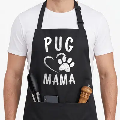 Pet puggle dog apron - White distressed PUG MAMA text with heart and paw print graphic — shown on a black cotton canvas apron against a white background