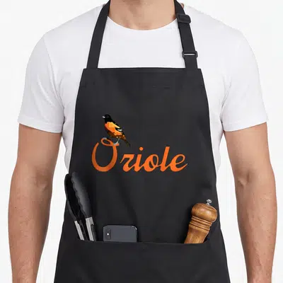 Cute oriole bird apron - Realistic orange and black bird perched on the letter O of the word Oriole — shown on a black cotton canvas apron against a white background