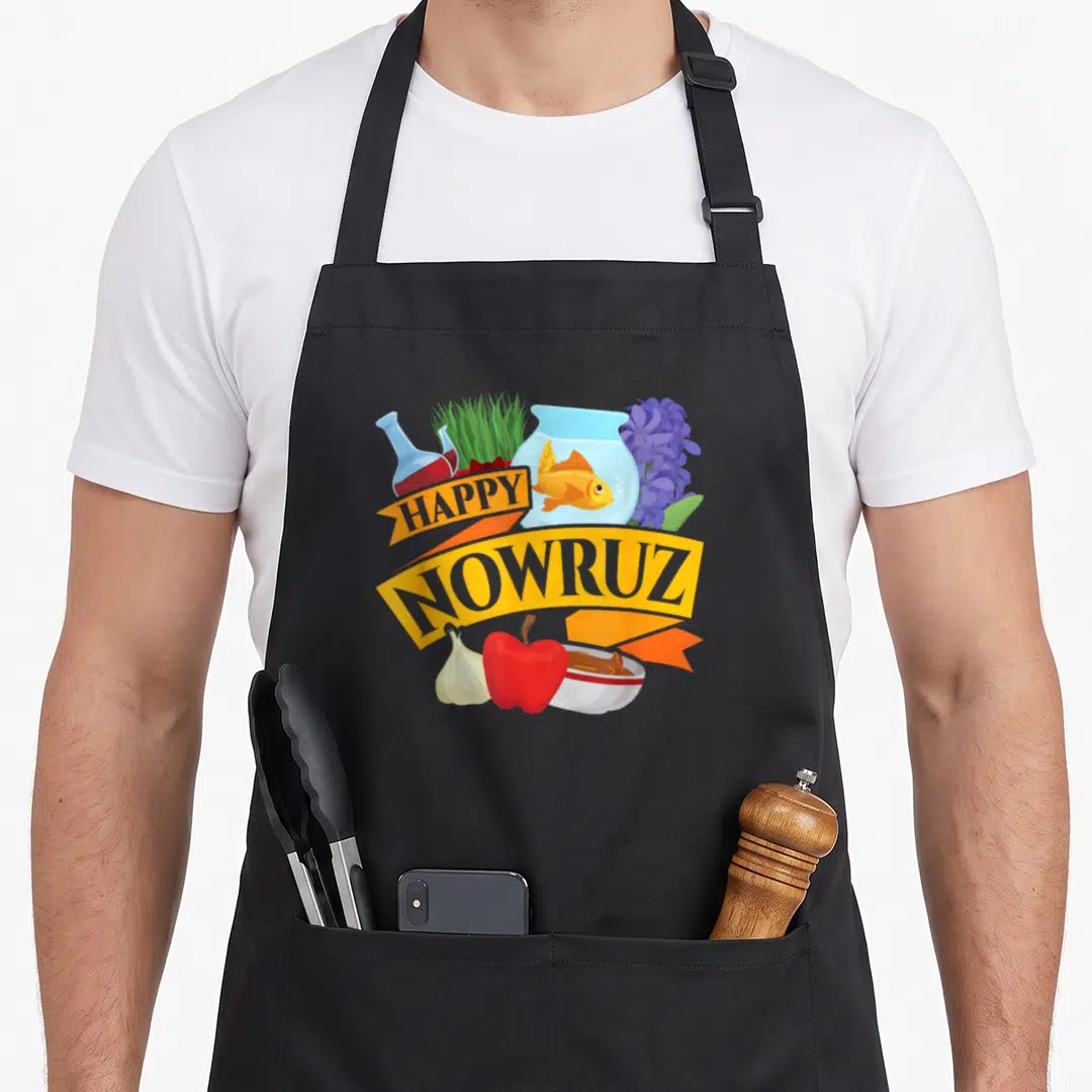 Persian cheers years apron - Yellow ribbon with Happy Nowruz text surrounded by fishbowl, grass, apple, garlic, bowl — shown on a black cotton canvas apron against a white background