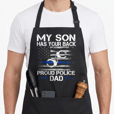Proud officer thin police apron - My Son Has Your Back text with handcuffs and distressed blue line flag — shown on a black cotton canvas apron against a white background