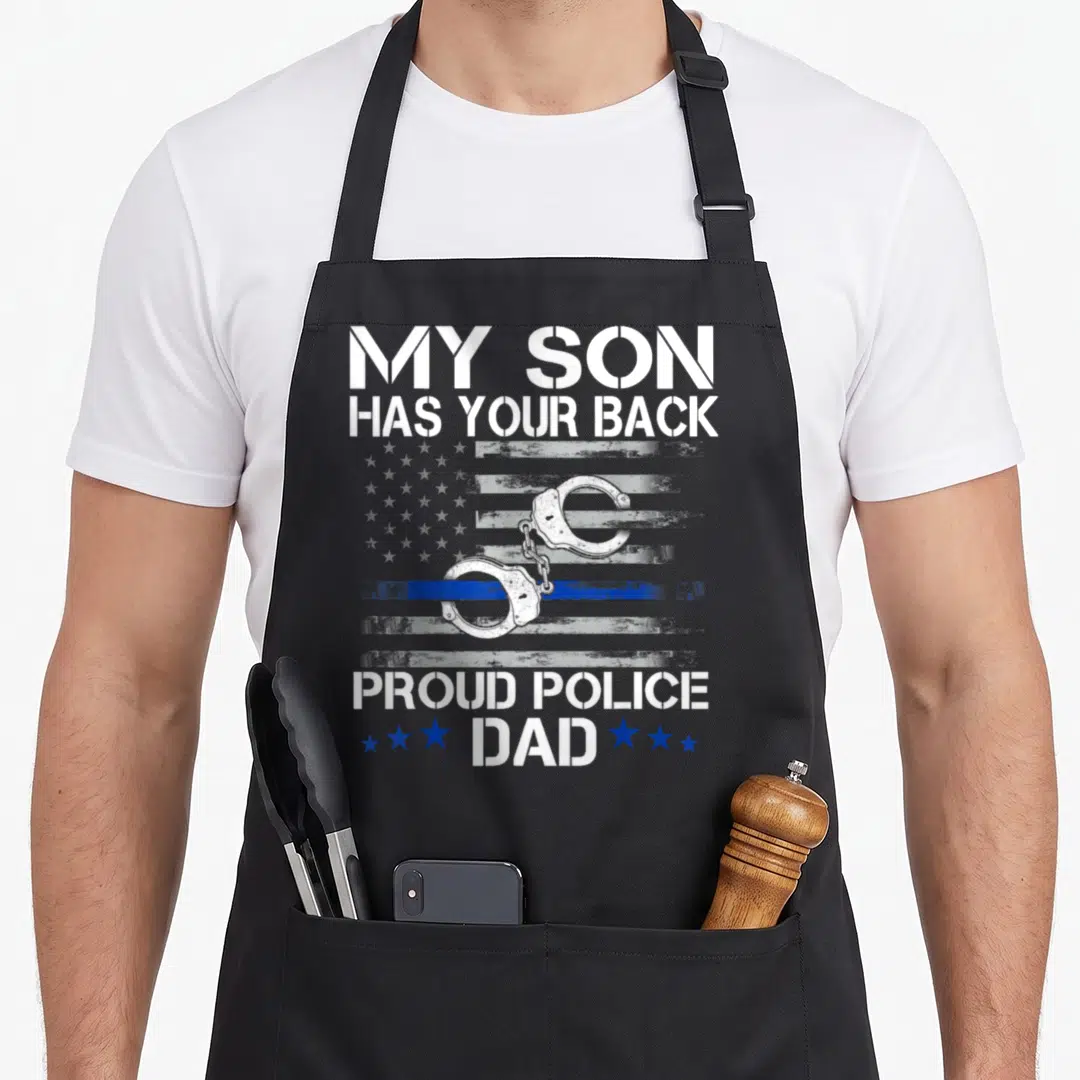 Proud officer thin police apron - My Son Has Your Back text with handcuffs and distressed blue line flag — shown on a black cotton canvas apron against a white background