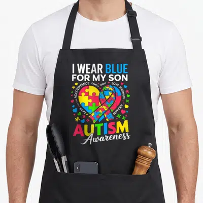 Awareness mom and son aprons - I WEAR BLUE FOR MY SON text with puzzle heart ribbon and support words — shown on a black cotton canvas apron against a white background