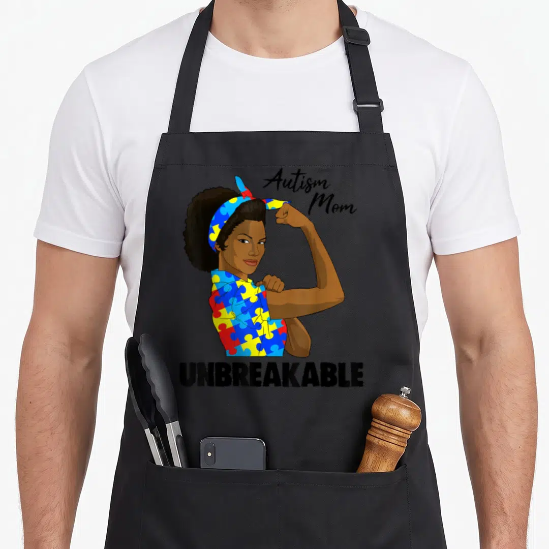 Autism special needs mom apron - Cartoon woman flexing arm wearing red blue yellow puzzle pattern clothes with Autism — shown on a black cotton canvas apron against a white background