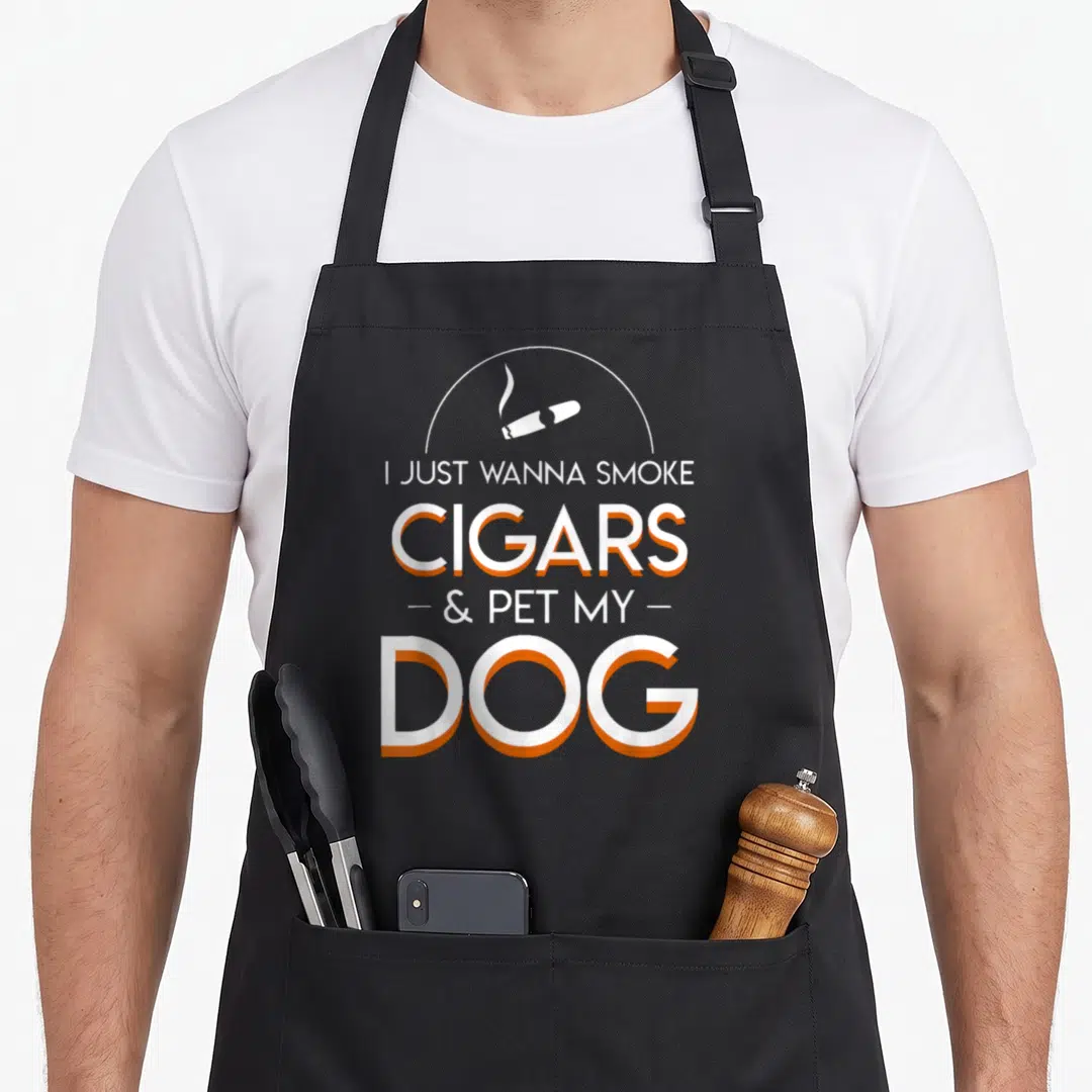 Smoke funny dog apron - I JUST WANNA SMOKE CIGARS & PET MY DOG text with cigar icon in white and orange — shown on a black cotton canvas apron against a white background