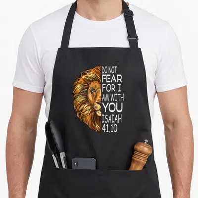 Fear bible verse apron - Realistic lion head illustration next to vertical Do Not Fear For I Am With You Isaiah 41.10 — shown on a black cotton canvas apron against a white background