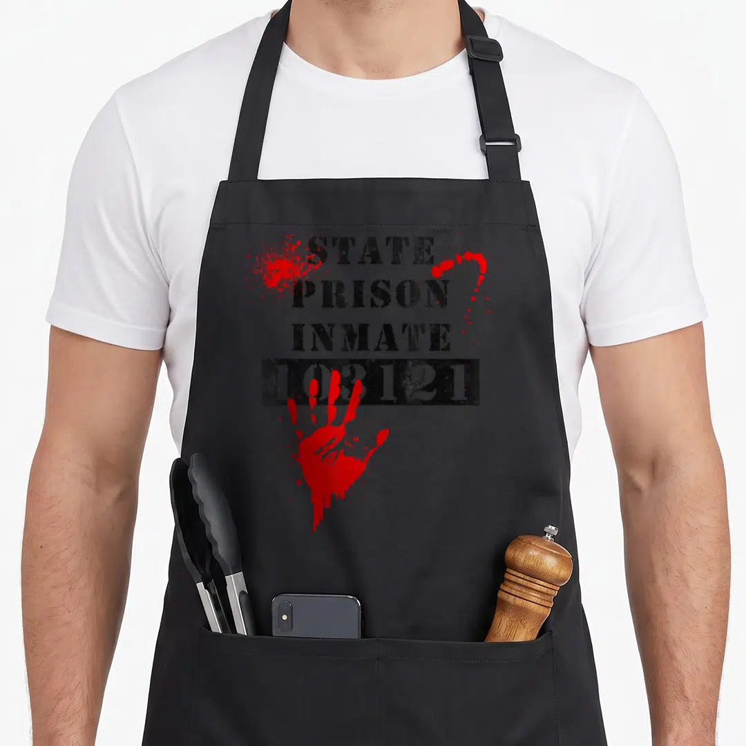 State bloody apron - STATE PRISON INMATE 103121 text and red handprint on black fabric — shown on a black cotton canvas apron against a white background