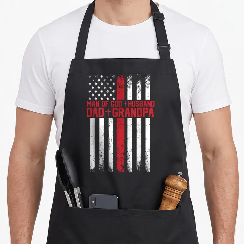 Cross god american flag apron - Distressed US flag with Man of God Husband Dad Grandpa text in red block letters — shown on a black cotton canvas apron against a white background