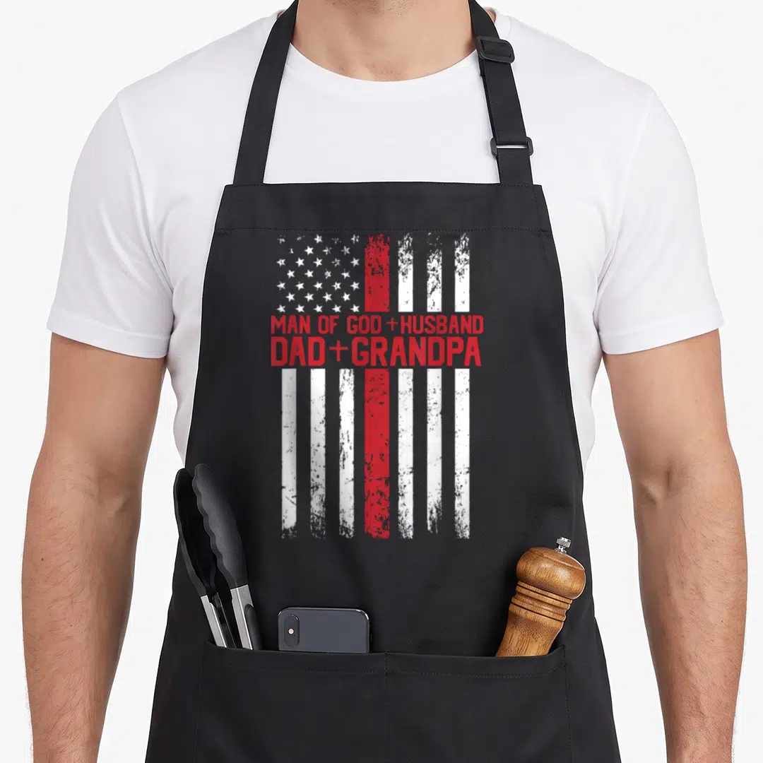 Cross god american flag apron - Distressed US flag with Man of God Husband Dad Grandpa text in red block letters — shown on a black cotton canvas apron against a white background