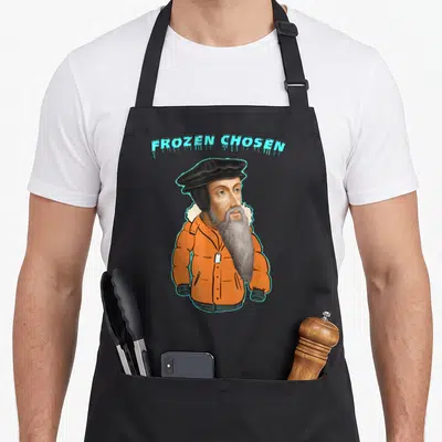 Calvinism tulip apron - FROZEN CHOSEN text above bearded man in orange puffer jacket and black hat — shown on a black cotton canvas apron against a white background
