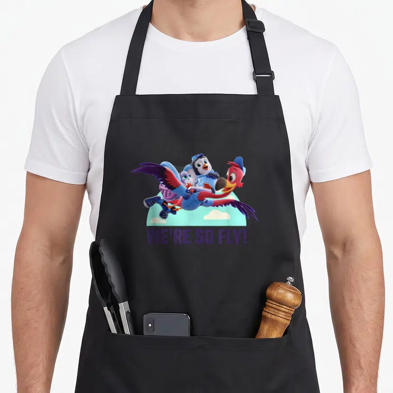 Fly junior apron - Three cartoon birds flying over clouds with We're So Fly text — shown on a black cotton canvas apron against a white background