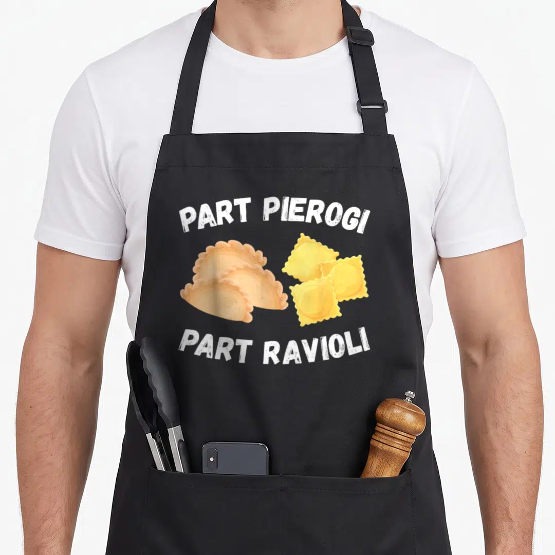 Polish italian aprons - Cartoon pierogi and ravioli with arched text Part Pierogi Part Ravioli in white tan and yellow — shown on a black cotton canvas apron against a white background