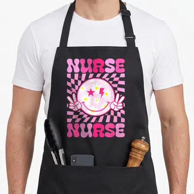 Future appreciation nurse apron - Retro smiley face with daisy eyes and peace signs flanked by stacked NURSE text — shown on a black cotton canvas apron against a white background