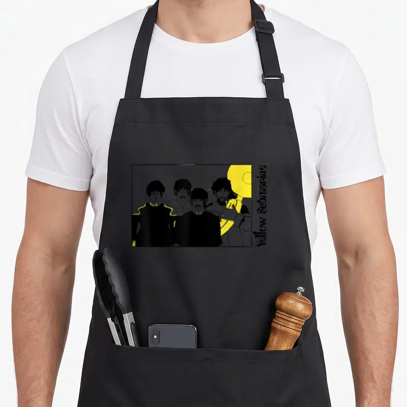 Funny tuba quotes apron - Four Beatles figures lined up with vertical Yellow Submarine text and yellow submarine graphic — shown on a black cotton canvas apron against a white background