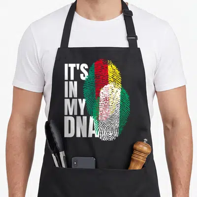 Cameroon heritage aprons - Stacked IT'S IN MY DNA text next to a fingerprint filled with red yellow green and white — shown on a black cotton canvas apron against a white background