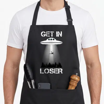 Alien abduction get loser apron - White UFO and beam lifting a silhouette above black trees with GET IN LOSER text — shown on a black cotton canvas apron against a white background