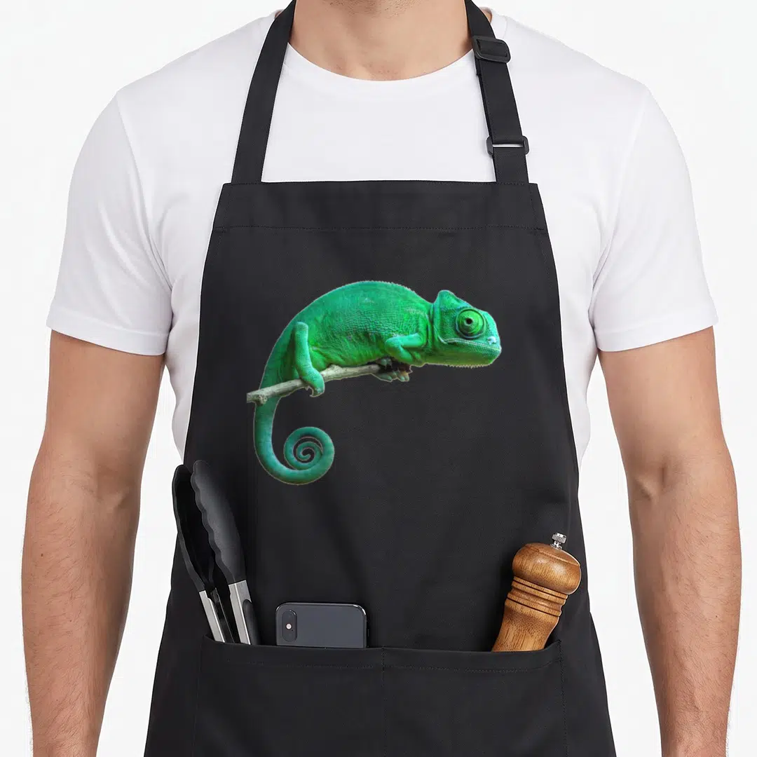 Lizard chameleon apron - Green chameleon perched on thin branch in photo style — shown on a black cotton canvas apron against a white background