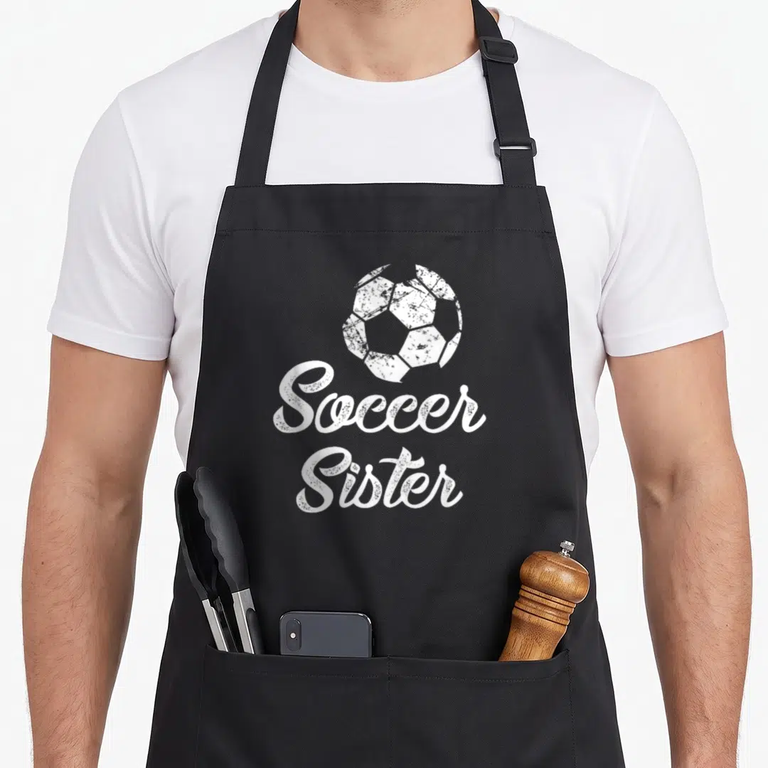 Sister soccer fan apron - Distressed white soccer ball above stacked cursive Soccer Sister text on black fabric — shown on a black cotton canvas apron against a white background