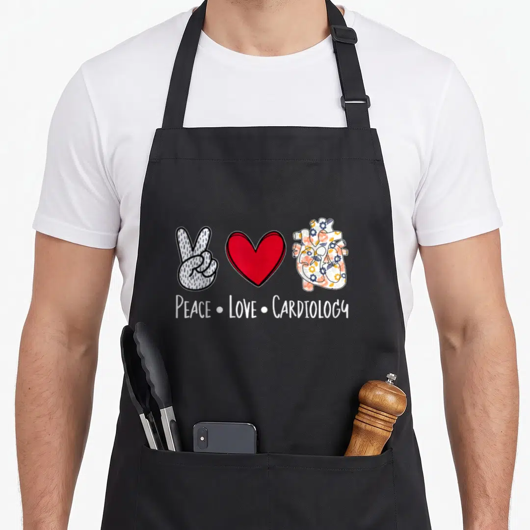 Peace cardiology nurse apron - Cartoon peace sign hand, red heart, and floral anatomical heart with text below — shown on a black cotton canvas apron against a white background