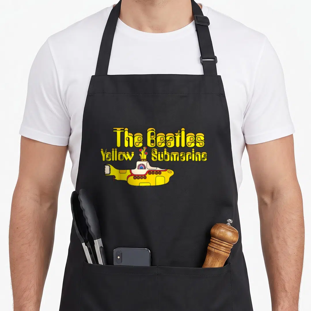 Cool yellow submarine apron - The Beatles Yellow Submarine cartoon text and yellow vessel with red and blue accents — shown on a black cotton canvas apron against a white background