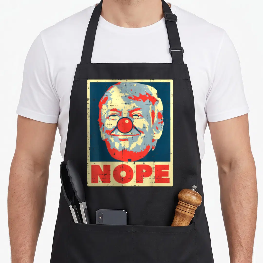 Nope clown aprons - Stylized man face with red nose in blue block above red NOPE text on cream background — shown on a black cotton canvas apron against a white background