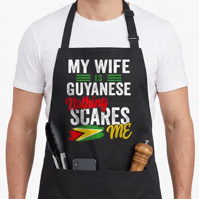 Guyana wife apron - My Wife Is Guyanese text with brush-stroke flag in white green red and yellow — shown on a black cotton canvas apron against a white background