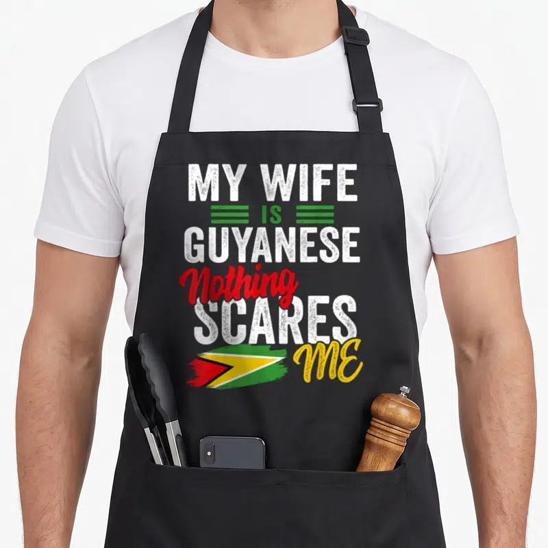 Guyana wife apron - My Wife Is Guyanese text with brush-stroke flag in white green red and yellow — shown on a black cotton canvas apron against a white background