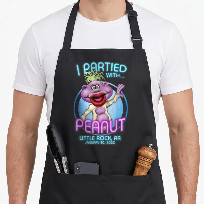 Rock funny peanut apron - Purple monster with I PARTIED WITH PEANUT text and Little Rock date — shown on a black cotton canvas apron against a white background