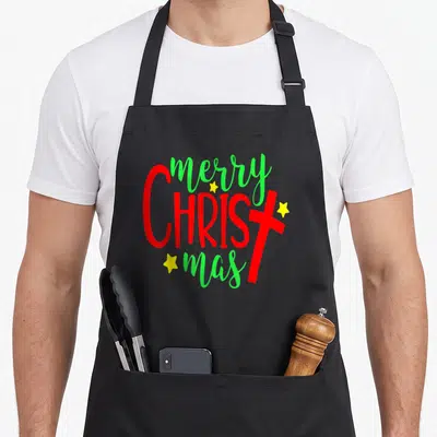 Costume merry christmas apron - Stacked red and green text with yellow stars and a red cross forming a Christmas message — shown on a black cotton canvas apron against a white background