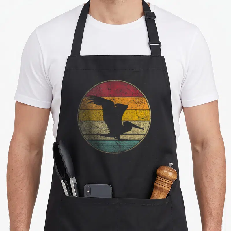 80s bird apron - Grey pelican silhouette over red orange yellow green grey retro stripes — shown on a black cotton canvas apron against a white background