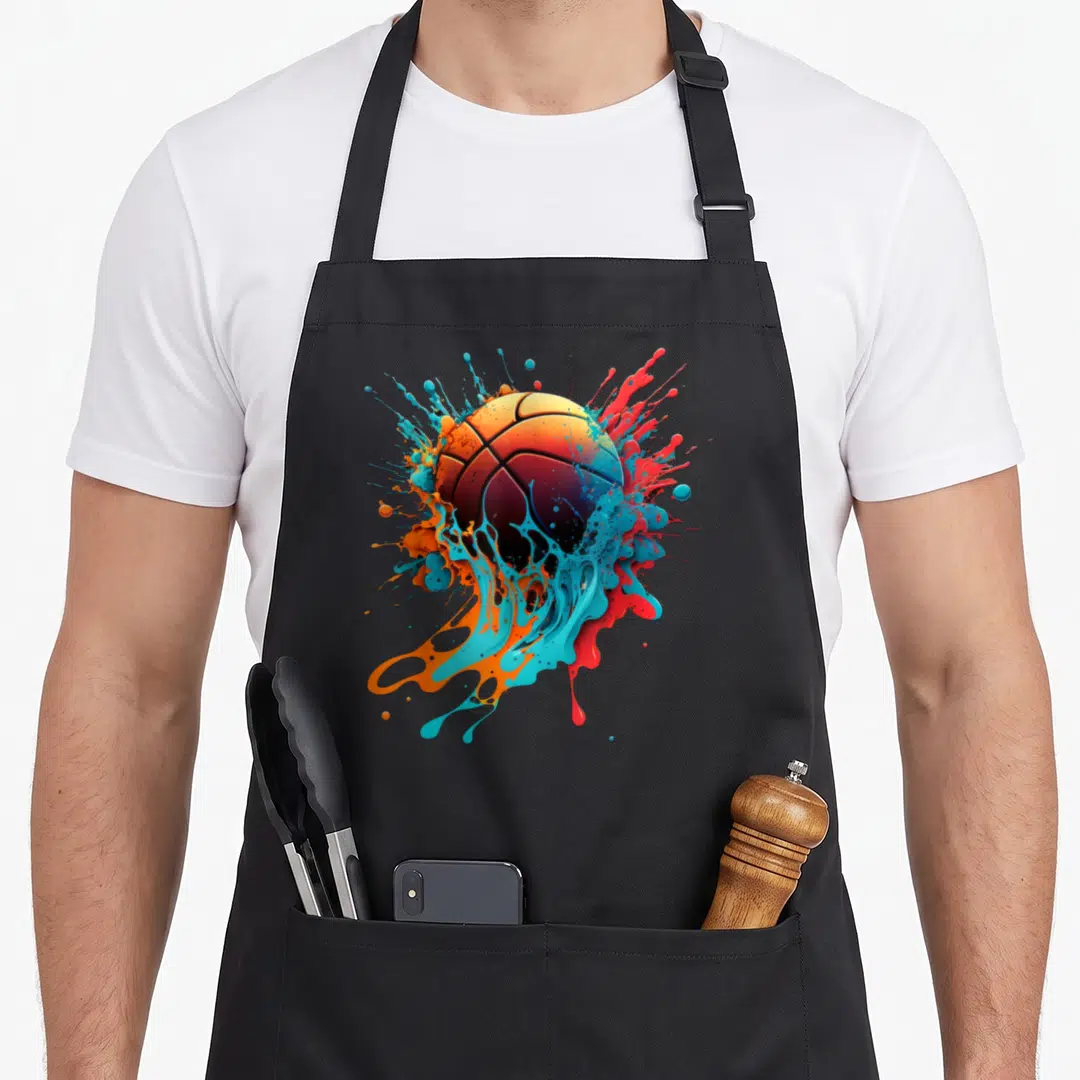 Basketball splash aprons - Realistic basketball surrounded by dripping splashes of blue, orange, red, and black paint — shown on a black cotton canvas apron against a white background