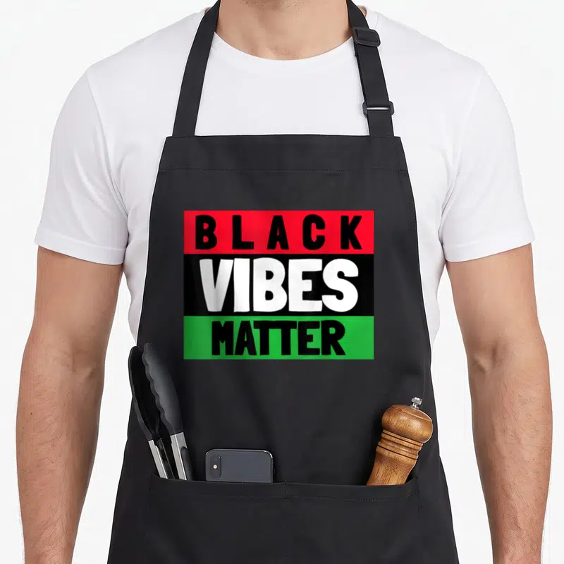 Matter black apron - Stacked BLACK VIBES MATTER text on red, black, and green horizontal stripes — shown on a black cotton canvas apron against a white background