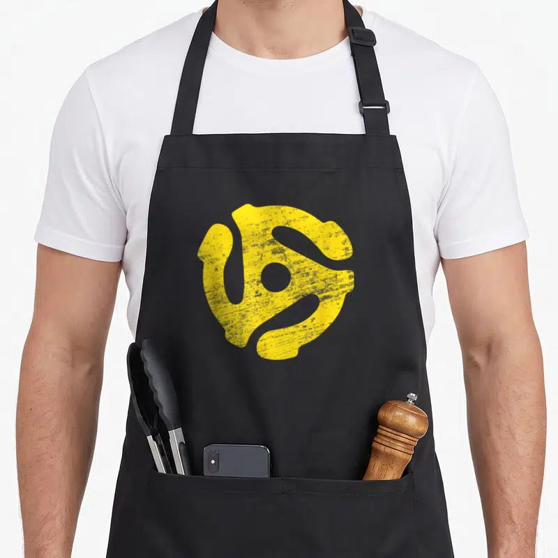 Rpm vinyl apron - Yellow distressed 45 RPM spindle adapter shape on grey background — shown on a black cotton canvas apron against a white background