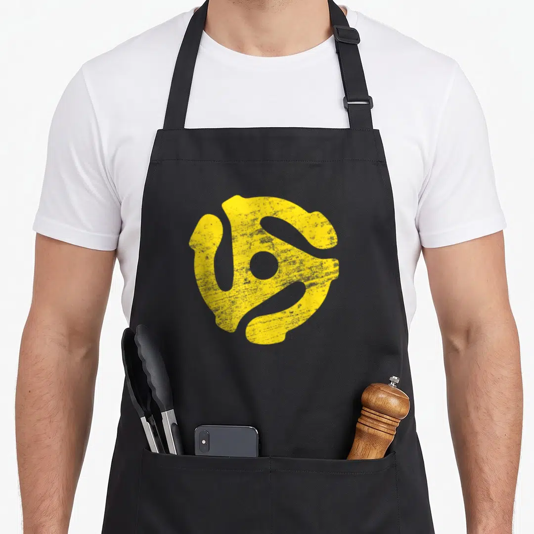 Rpm vinyl apron - Yellow distressed 45 RPM spindle adapter shape on grey background — shown on a black cotton canvas apron against a white background