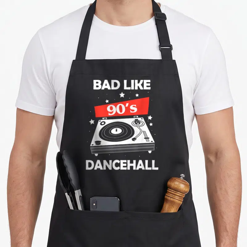 Dancehall 90s apron - Retro turntable with BAD LIKE text, red 90s banner, and white stars on grey background — shown on a black cotton canvas apron against a white background