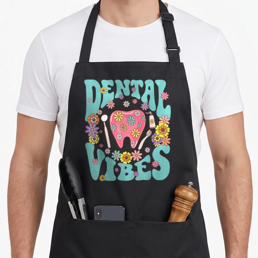 Groovy dentist apron - DENTAL VIBES text surrounding a pink floral tooth with a mirror and toothbrush — shown on a black cotton canvas apron against a white background