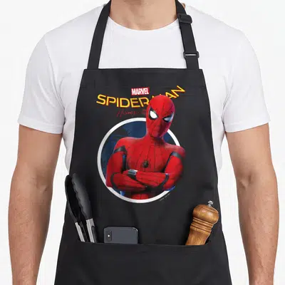 Homecoming cross apron - Spider-Man with crossed arms in red suit inside white circle with blue cityscape and stacked — shown on a black cotton canvas apron against a white background