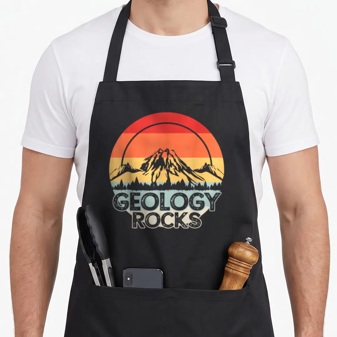 Geology rock geologist apron - Retro circular sunset with grey mountain and forest, stacked GEOLOGY ROCKS text below — shown on a black cotton canvas apron against a white background