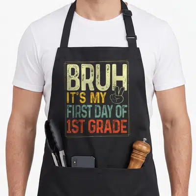 1st bruh grade apron - Stacked text reading Bruh Its My First Day Of 1st Grade with peace sign outline in beige yellow — shown on a black cotton canvas apron against a white background