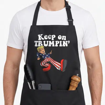 Trumpin funny butter apron - Stacked text Keep on Trumpin above a dancing cartoon figure in a flag suit — shown on a black cotton canvas apron against a white background