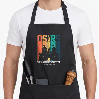 Commerce e.a apron - Multi-colored OSRS text with castle silhouette and Straight Outta Lumbridge caption — shown on a black cotton canvas apron against a white background