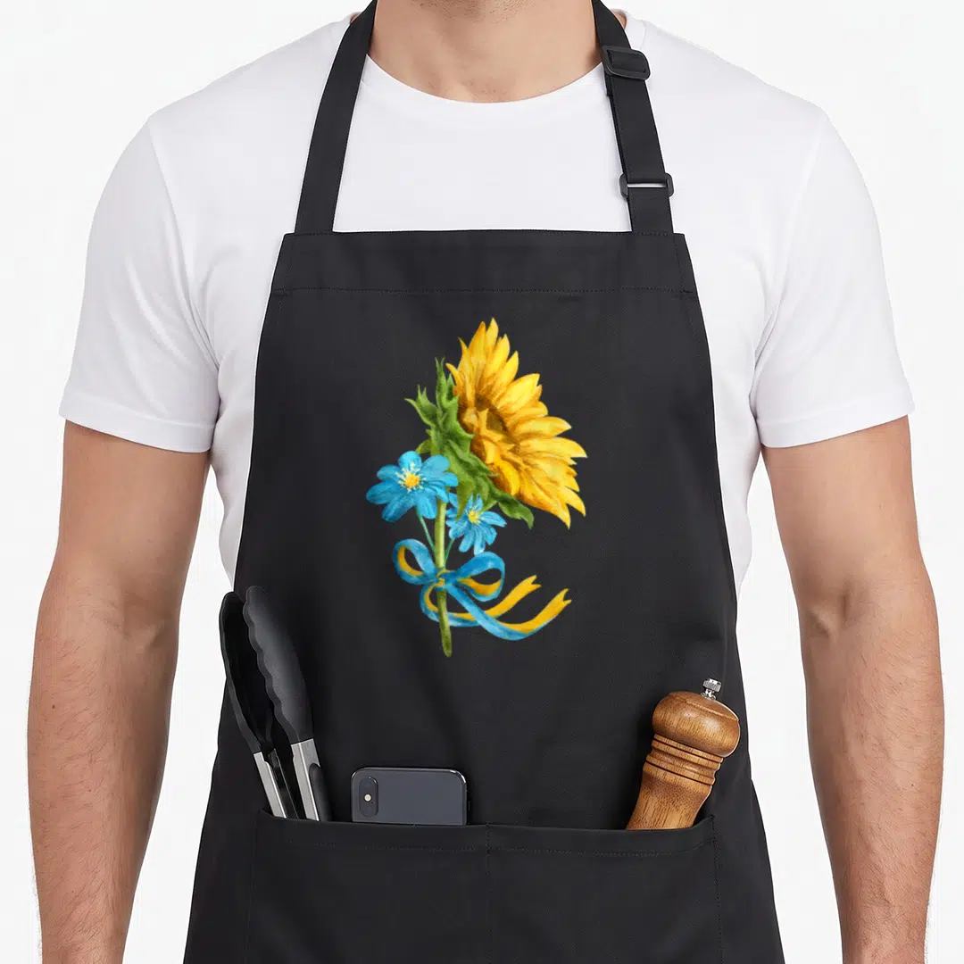 Ukraine sunflower apron - Yellow sunflower and two blue flowers with a blue and yellow ribbon in watercolor style — shown on a black cotton canvas apron against a white background