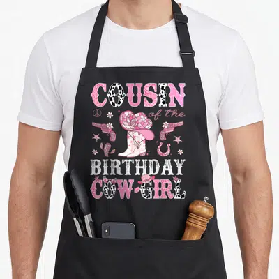 Cousin cowgirl aprons - Pink western birthday design with cowboy hat boots revolvers cactus and stars on canvas — shown on a black cotton canvas apron against a white background