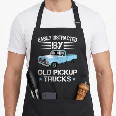 Distracted truck apron - Light blue vintage pickup truck with white distressed text and two blue stars — shown on a black cotton canvas apron against a white background